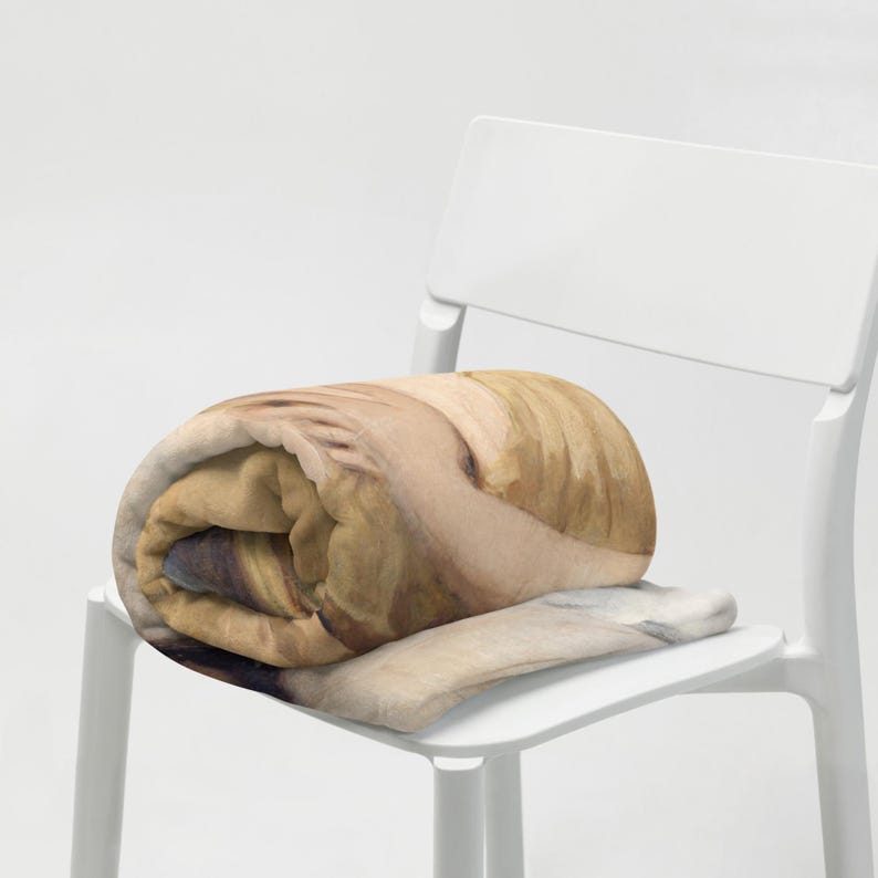 May include: A rolled blanket with a watercolour design in shades of tan, beige, and brown rests on a white chair. The blanket's pattern includes subtle colour variations, creating a soft, textured appearance. The chair has a minimalist design.