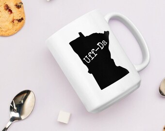 May include: White ceramic mug with a black silhouette of the state of Minnesota and the text "Uff-Da" printed on it.