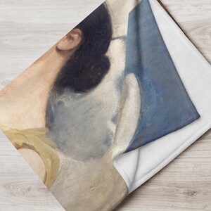 May include: A throw blanket with a detail from a classical painting. The design shows a woman's profile with dark hair, a yellow garment, and a blue background. The underside of the blanket is white.