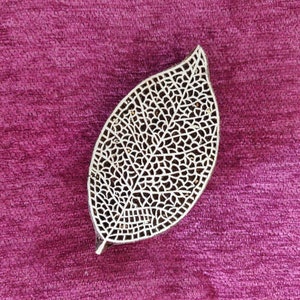 May include: A white wooden leaf-shaped block with a detailed, intricate design carved into it. The block is sitting on a deep pink fabric surface.