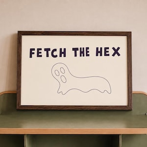 Könnte beinhalten: Ein rechteckiger gerahmter Druck mit dem Text FETCH THE HEX in dunkelvioletten Großbuchstaben über einer einfachen schwarzen Strichzeichnung eines Geistes mit langgestrecktem Körper und drei ovalen Öffnungen für Augen und Mund auf weißem Grund.