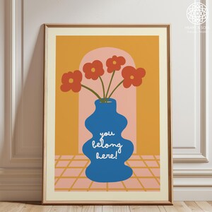 Può includere: Stampa artistica incorniciata con un vaso blu con fiori rossi su sfondo arancione. Il vaso riporta la scritta "you belong here!". La stampa ha uno stile retrò e minimalista.