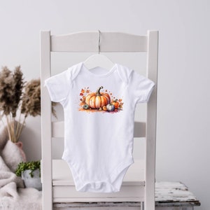 May include: White baby onesie featuring a watercolour illustration of pumpkins and autumn leaves. The pumpkins are orange and the leaves are red, orange, and yellow.