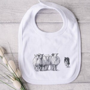 May include: White baby bib with a black and white illustration of sheep and a border collie dog. The bib has a rounded shape with a neck opening at the top. The sheep are standing together, and the dog is running towards them.