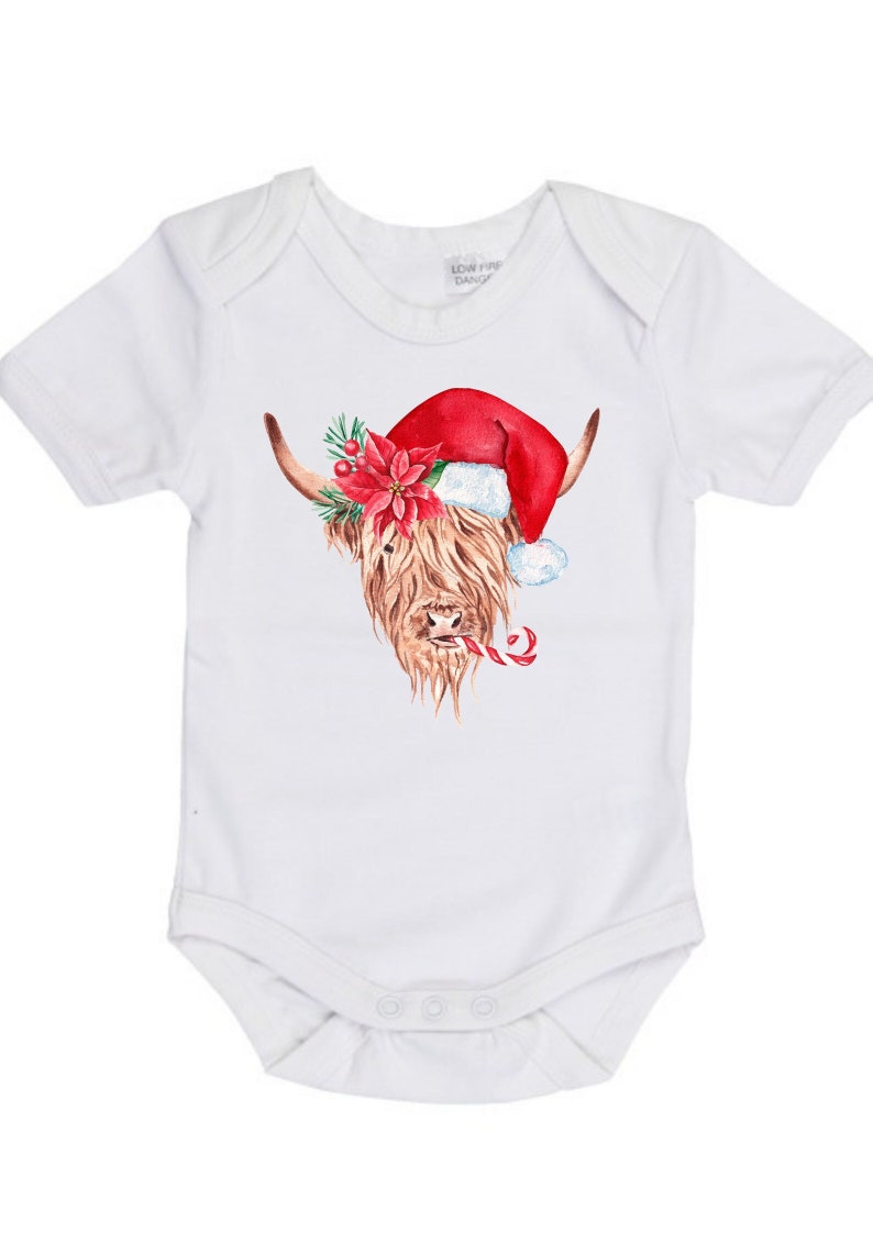 May include: White baby onesie featuring a Christmas-themed illustration of a Highland cow wearing a Santa hat and holding a candy cane.