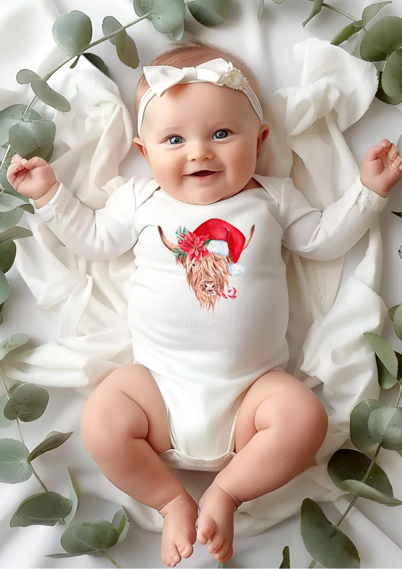 May include: A white baby onesie with a long sleeve design features a brown and white Highland cow wearing a red Santa hat. The cow is surrounded by red and green holly and a candy cane.