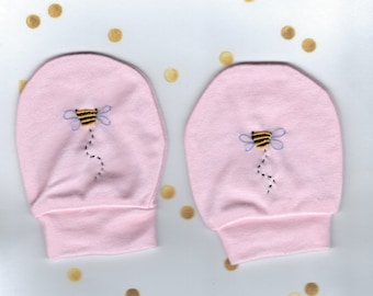 May include: A pair of pink baby mittens with embroidered bee designs. The bees are yellow and black with blue wings.