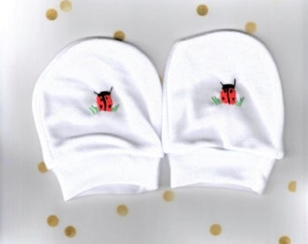 May include: A pair of white baby mittens with red ladybug embroidery. The mittens are made of soft cotton and are perfect for keeping baby's hands warm and protected.