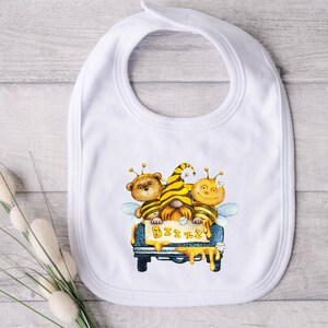 May include: White baby bib featuring a yellow, black and brown bee-themed design. Three cartoon bees are riding in a blue truck with a sign that says "BZZZZ".