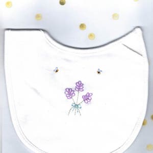 May include: White cotton bib with embroidered lavender flowers and bees in purple, blue, and green.