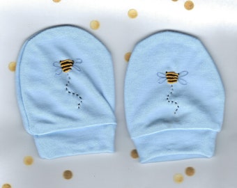 May include: A pair of light blue baby mittens with embroidered bees. The bees are yellow and black with a black outline.