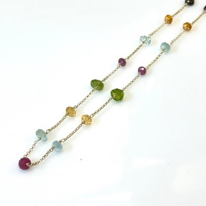 Puede incluir: Un collar de cadena de oro con una variedad de cuentas de piedras preciosas. Las cuentas son en tonos de verde, azul, amarillo y rojo.