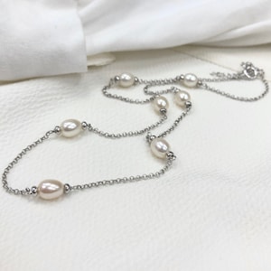 May include: A silver chain necklace with five white oval pearls. The necklace is on a white surface.