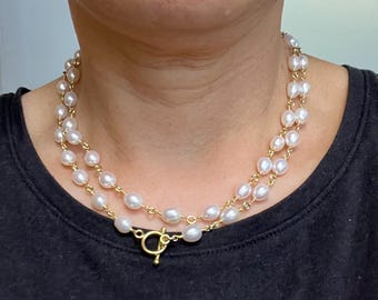May include: A white pearl necklace with a gold clasp. The necklace is layered and has a simple design.