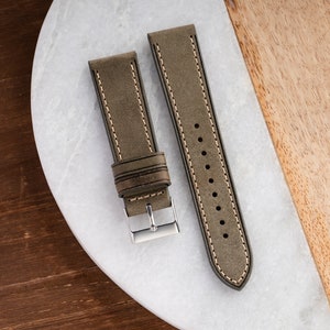 Pu&ograve; includere: Due cinturini per orologio in pelle marrone con cuciture bianche. I cinturini sono su una superficie di marmo bianco.