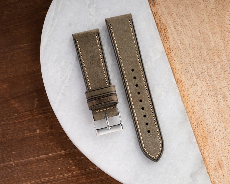 Pu&ograve; includere: Due cinturini per orologio in pelle marrone con cuciture bianche. I cinturini sono su una superficie di marmo bianco.