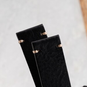 K&ouml;nnte beinhalten: Nahaufnahme von zwei schwarzen Leder-Uhrenarmb&auml;ndern mit beigen N&auml;hten. Die Armb&auml;nder sind rechteckig mit abgerundeten Ecken und einer strukturierten Oberfl&auml;che. Die N&auml;hte sind oben an jedem Armband sichtbar und setzen einen Kontrast.