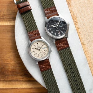 May include: Two silver wristwatches with different faces and green nylon watch bands. The watch on the left has a cream-colored face with black markings and the text "THU 128". The watch on the right has a black face with silver markings and the text "SEIKO 5".