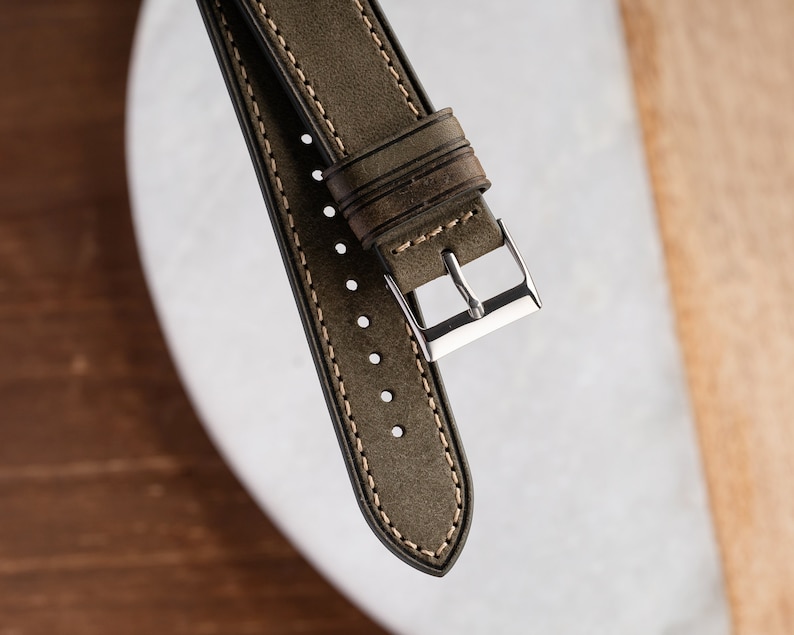 Pu&ograve; includere: Un cinturino per orologio in pelle verde con cuciture bianche e una fibbia argentata.