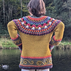 May include: A crocheted sweater with a colorful yoke design. The sweater is a mustard yellow color with a multi-colored yoke featuring a geometric pattern. The sweater has long sleeves and a loose fit.