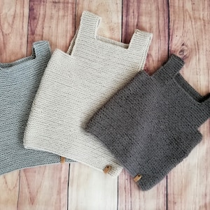 Könnte beinhalten: Drei gestrickte ärmellose Oberteile in verschiedenen Farben: Grau, Beige und Braun. Die Oberteile sind aus einem weichen, strukturierten Garn gefertigt und haben ein schlichtes, klassisches Design.
