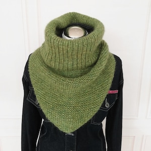 Könnte beinhalten: Ein grüner gestrickter Schal mit Rollkragen und dreieckiger Form. Der Schal ist aus weichem, flauschigem Garn gefertigt und perfekt, um sich im Winter warm zu halten.