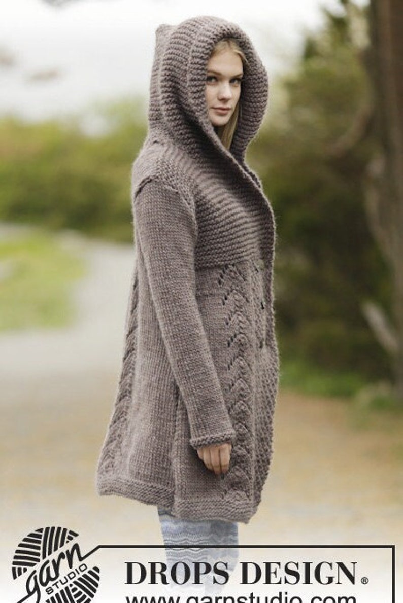 May include: A long, brown knitted cardigan with a hood and a lace pattern on the front. The cardigan is open in the front and has a relaxed fit. The text "DROPS DESIGN." is visible at the bottom of the image.