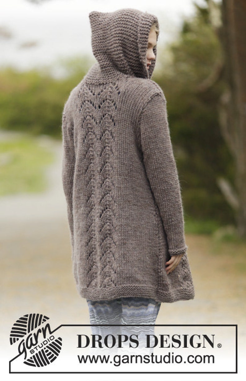 May include: A brown hooded cardigan with a lacy back detail. The cardigan is long and has a relaxed fit. The model is wearing the cardigan with a pair of striped pants. DROPS DESIGN www.garnstudio.com