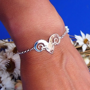 May include: A silver bracelet with a ram's head charm. The bracelet is on a person's wrist and the charm is centered on the wrist.