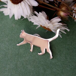 K&ouml;nnte beinhalten: Eine silberne Katzen-Silhouettennadel auf gr&uuml;nem Hintergrund. Die Nadel ist ein schlichtes, modernes Design und w&auml;re ein tolles Geschenk f&uuml;r Katzenliebhaber.