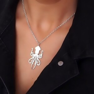 May include: A silver necklace with a detailed octopus pendant. The necklace is worn by a person with a black jacket.