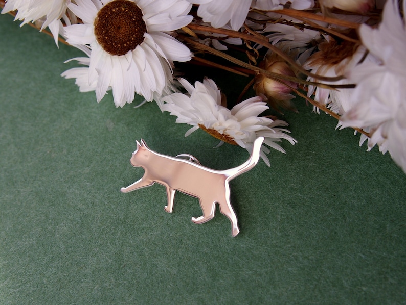 K&ouml;nnte beinhalten: Eine silberne Katzen-Silhouettennadel auf gr&uuml;nem Hintergrund. Die Nadel ist ein schlichtes, modernes Design und w&auml;re ein tolles Geschenk f&uuml;r Katzenliebhaber.