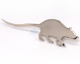 Könnte beinhalten: Eine silberne Rattenbrosche mit einem detaillierten Silhouettendesign. Die Ratte ist in einer laufenden Pose mit ausgestrecktem Schwanz dargestellt.