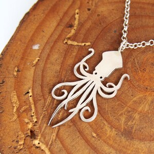 May include: A silver necklace with a squid pendant. The pendant is a cutout design of a squid with tentacles.