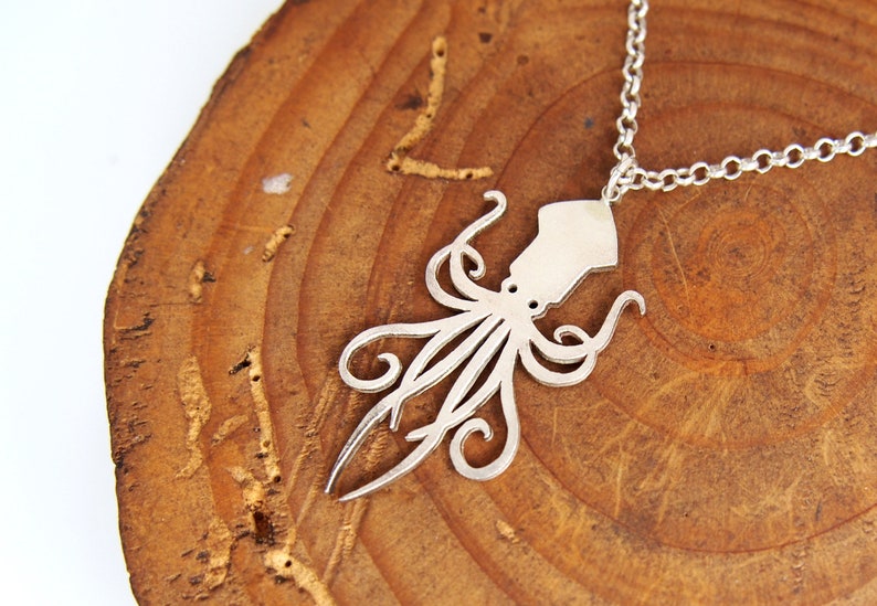 May include: A silver necklace with a squid pendant. The pendant is a cutout design of a squid with tentacles.