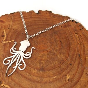 May include: A silver necklace with a detailed cutout of an octopus pendant. The necklace is displayed on a wooden surface.