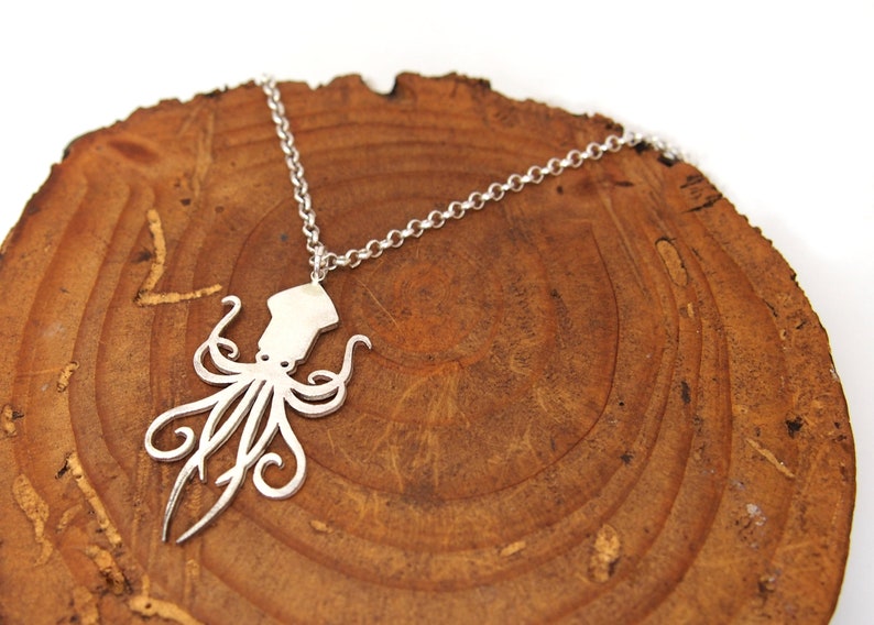 May include: A silver necklace with a detailed cutout of an octopus pendant. The necklace is displayed on a wooden surface.