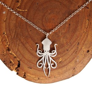 May include: A silver necklace with a detailed cutout of an octopus pendant. The necklace is displayed on a wooden surface.