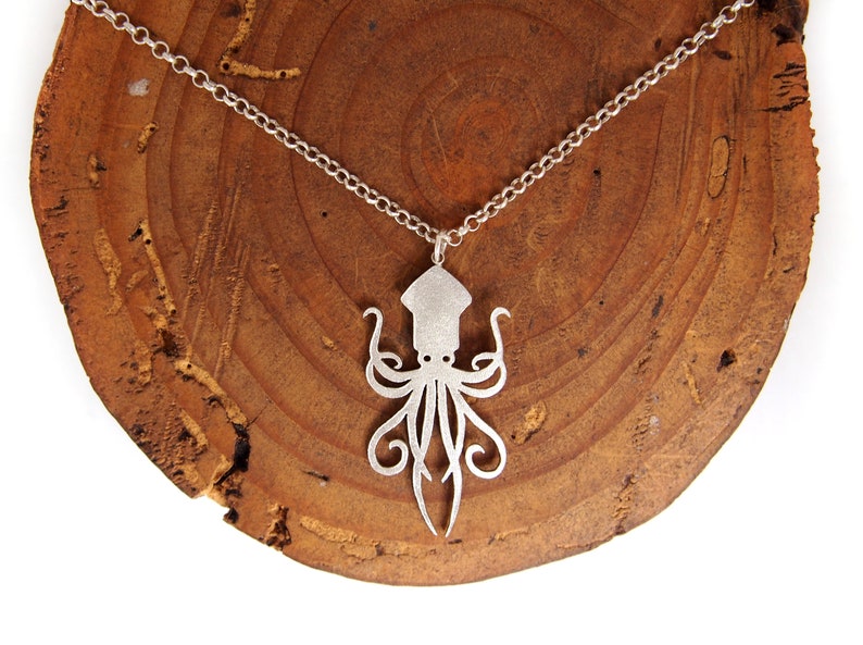 May include: A silver necklace with a detailed cutout of an octopus pendant. The necklace is displayed on a wooden surface.