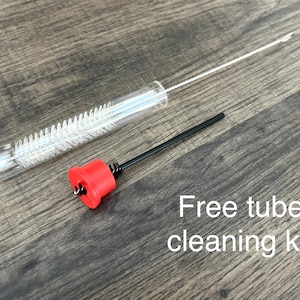 May include: A clear glass tube with a white brush inside, a black rod with a red cap, and the text "Free tube cleaning kit" on a wooden surface. The cleaning kit is designed for small tubes.