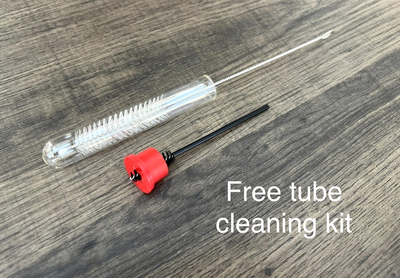 May include: A clear glass tube with a white brush inside, a black rod with a red cap, and the text "Free tube cleaning kit" on a wooden surface. The cleaning kit is designed for small tubes.