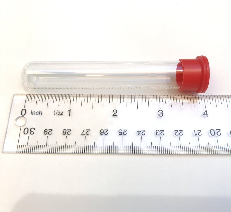 May include: A clear, cylindrical test tube with a red cap, approximately 4 inches long, is positioned next to a ruler. The ruler shows inch measurements. The tube is empty and made of transparent material.