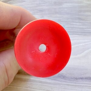 May include: A bright red, circular object with a central hole. The object appears to be made of plastic or a similar material. The surface is smooth and the color is solid. The object is likely a component of a larger item.