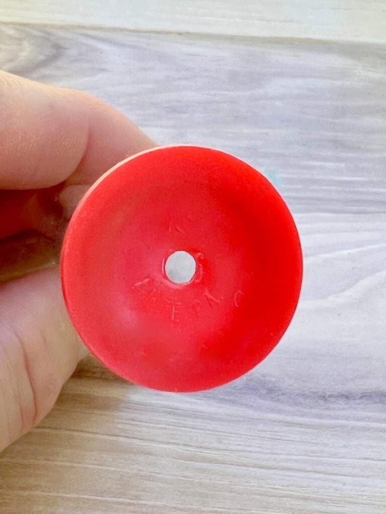 May include: A bright red, circular object with a central hole. The object appears to be made of plastic or a similar material. The surface is smooth and the color is solid. The object is likely a component of a larger item.