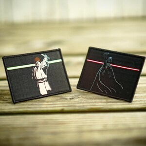 May include: Two black fabric patches with embroidered images of Star Wars characters. The left patch features Luke Skywalker holding a lightsaber with a green blade. The right patch features Darth Vader holding a lightsaber with a red blade.