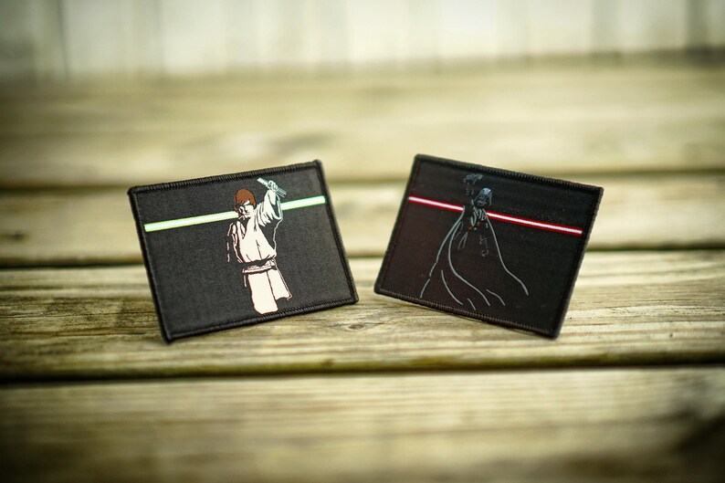 May include: Two black fabric patches with embroidered images of Star Wars characters. The left patch features Luke Skywalker holding a lightsaber with a green blade. The right patch features Darth Vader holding a lightsaber with a red blade.