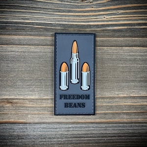 Könnte beinhalten: Ein schwarzer und grauer Patch mit einem Design aus drei Kugeln und dem Text "FREEDOM BEANS".