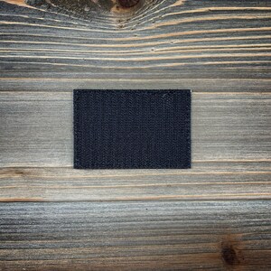 K&ouml;nnte beinhalten: Ein schwarzer Klettverschluss-Patch, auch bekannt als Velcro-Patch, auf einem Holzgrund.