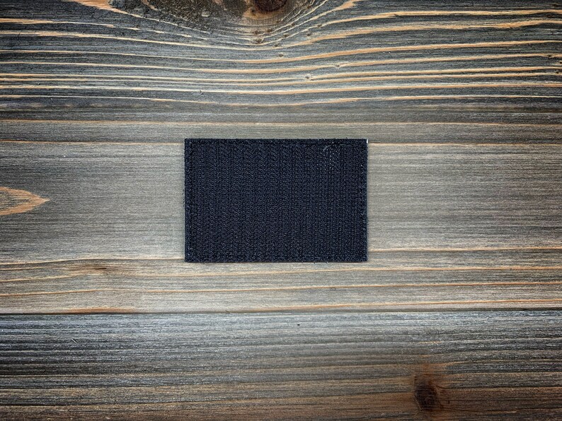 K&ouml;nnte beinhalten: Ein schwarzer Klettverschluss-Patch, auch bekannt als Velcro-Patch, auf einem Holzgrund.