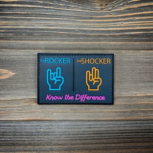 May include: Black patch with white stitching, featuring two hand gestures, one in blue and one in orange, with the text "the ROCKER" and "the SHOCKER" above each hand. The text "Know the Difference" is written in pink below the hands.